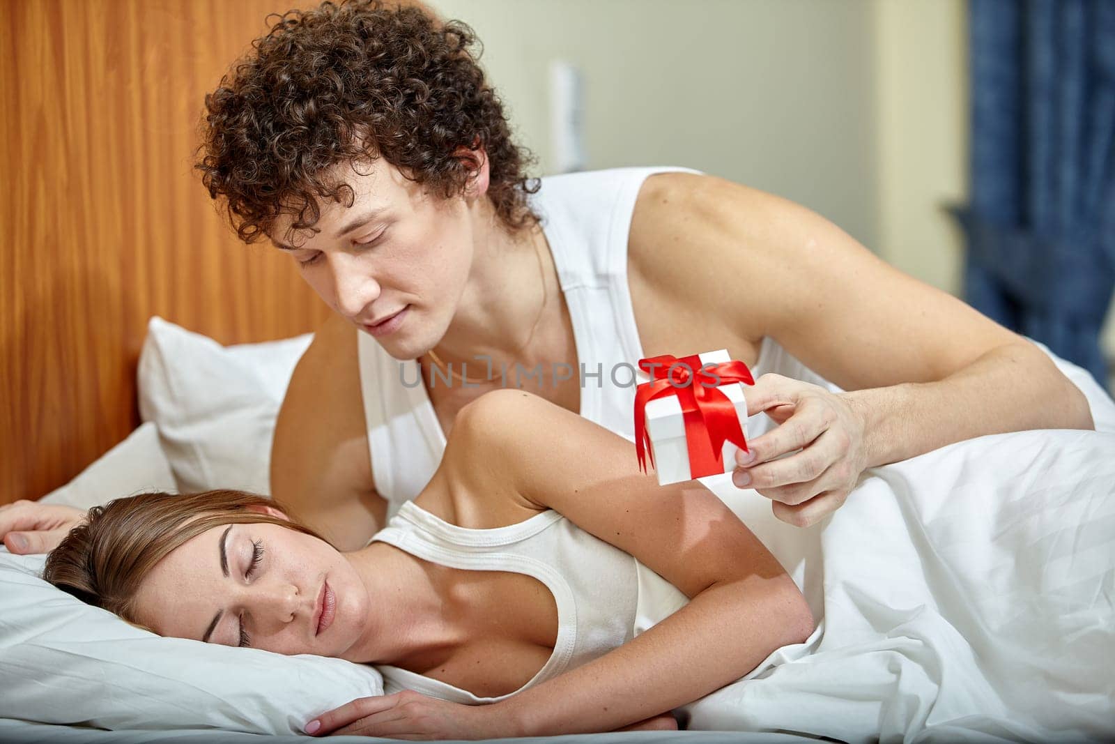 Happy young family with gift box lies in the bed at home. Valentine's Day