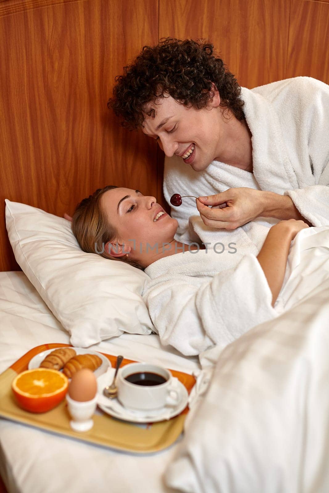 Happy young family  with breakfast lies in the bed at home.