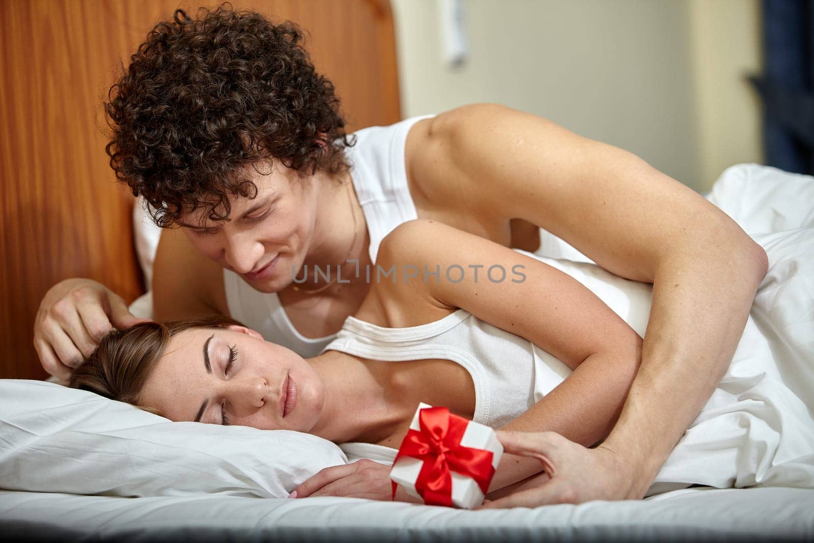Happy young family with gift box lies in the bed at home. Valentine's Day