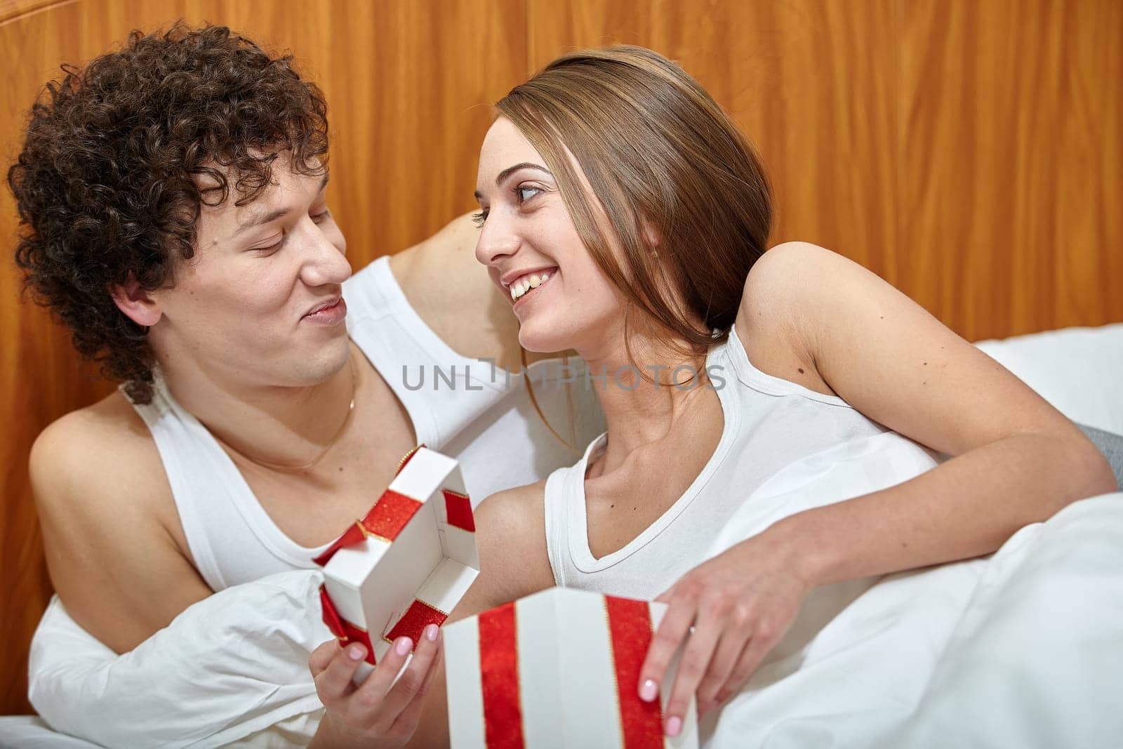 Happy young family with gift box lies in the bed at home. Valentine's Day