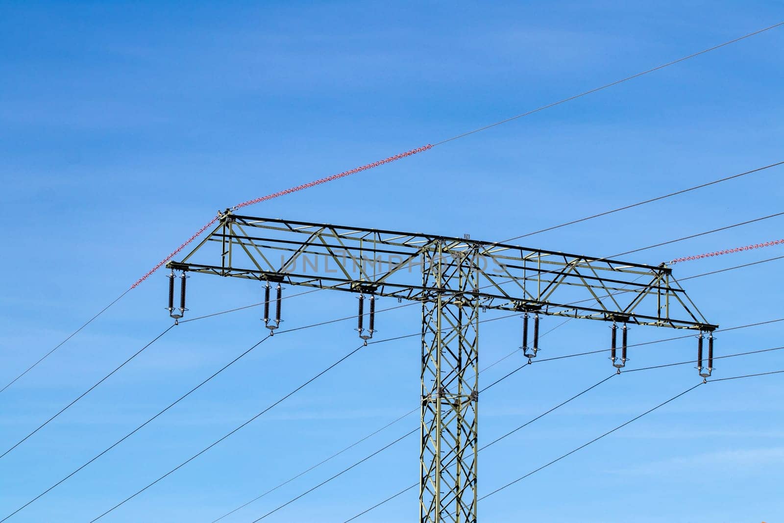 Electric power transmission concept. Selective focus on a electricity supply pylon and the high voltage power lines against a blue cloudy sky.