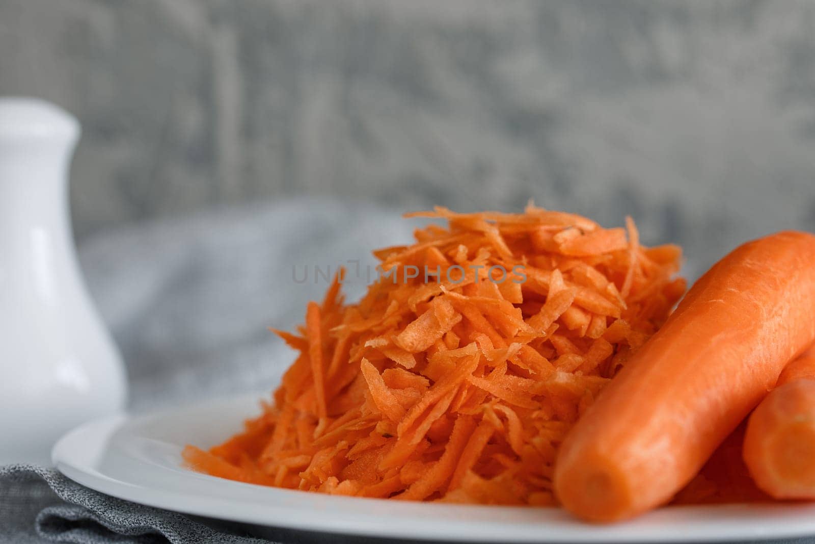 Grated carrots on a white plate and two whole carrots nearby