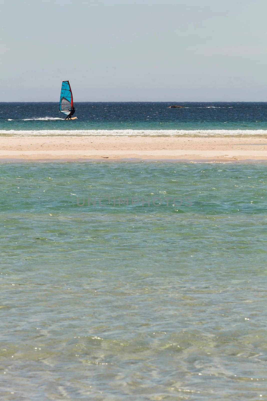 Windsurfer sailing near the sand of the beach with turquoise water in the foreground