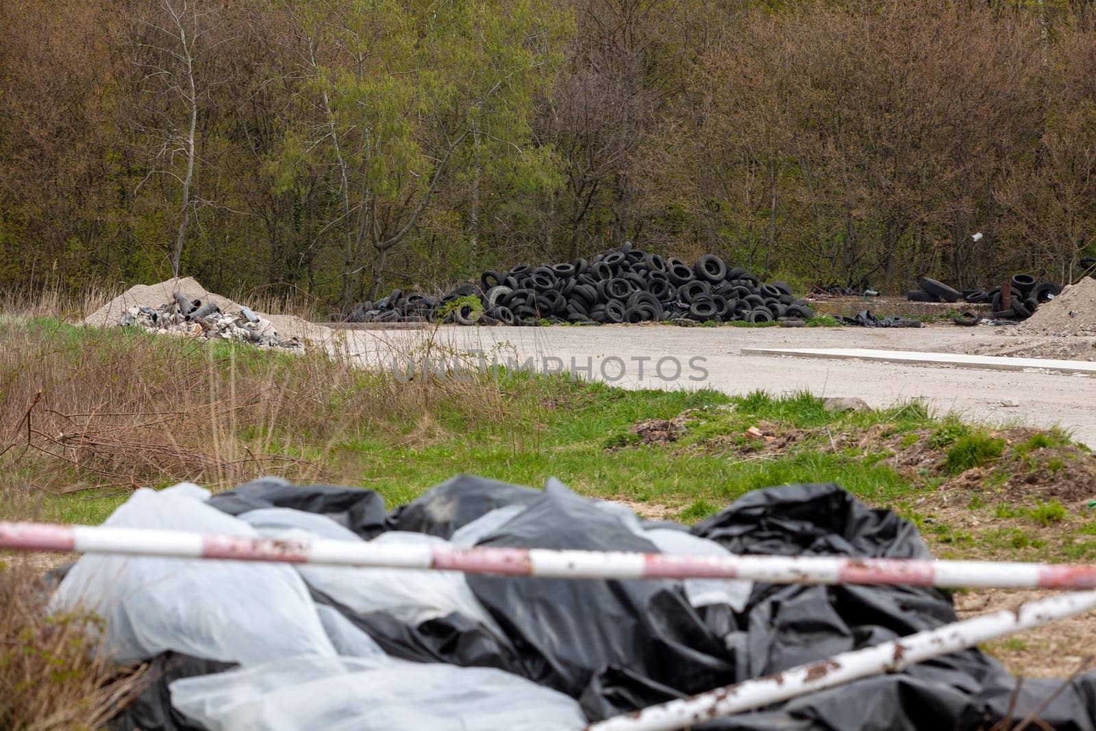 Illegal dump near the country road in the country on sunny day. Trash pollution in the nature. Dirty dump near the forest woods.