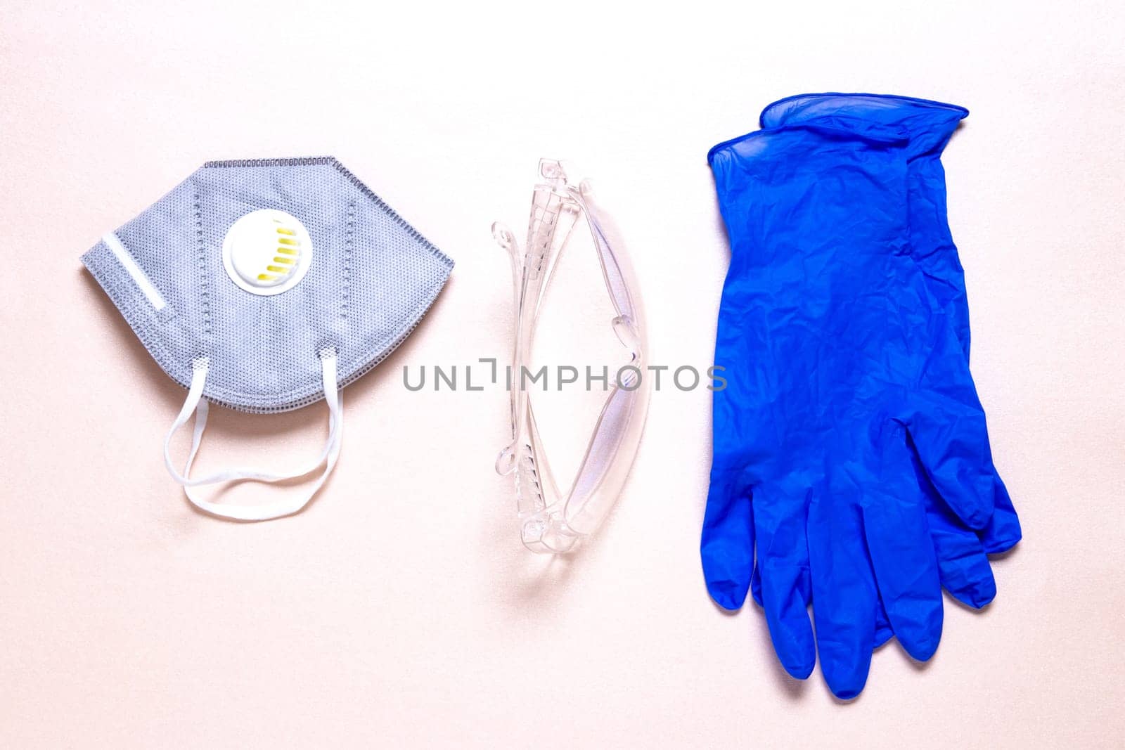 Coronavirus protective measures. Close-up of a N95 face mask or particle filtering half mask, a clear transparent safety glasses and medical gloves on a sparkling light pink paper background. Personal protective equipment.