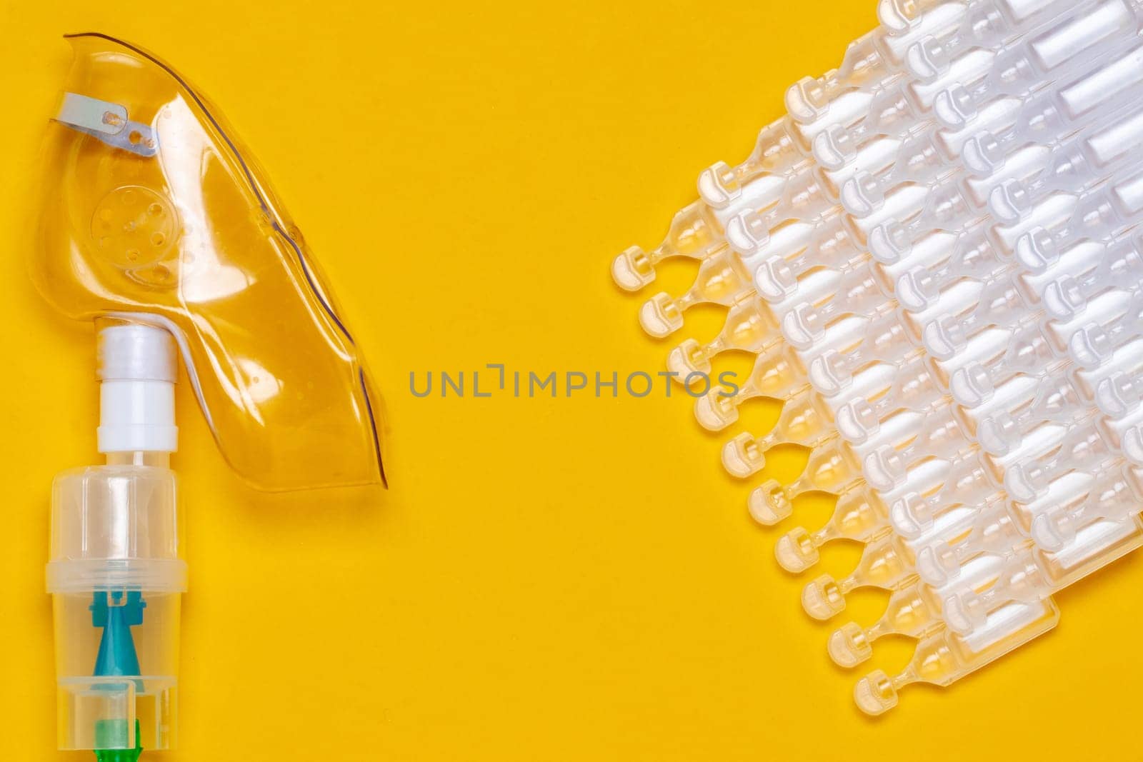 Coronavirus treatment concept. A medical face mask or nebulizer for treatment of the respiratory tract and several tens packs of ampoules flat layed on a yellow background. Copy space.