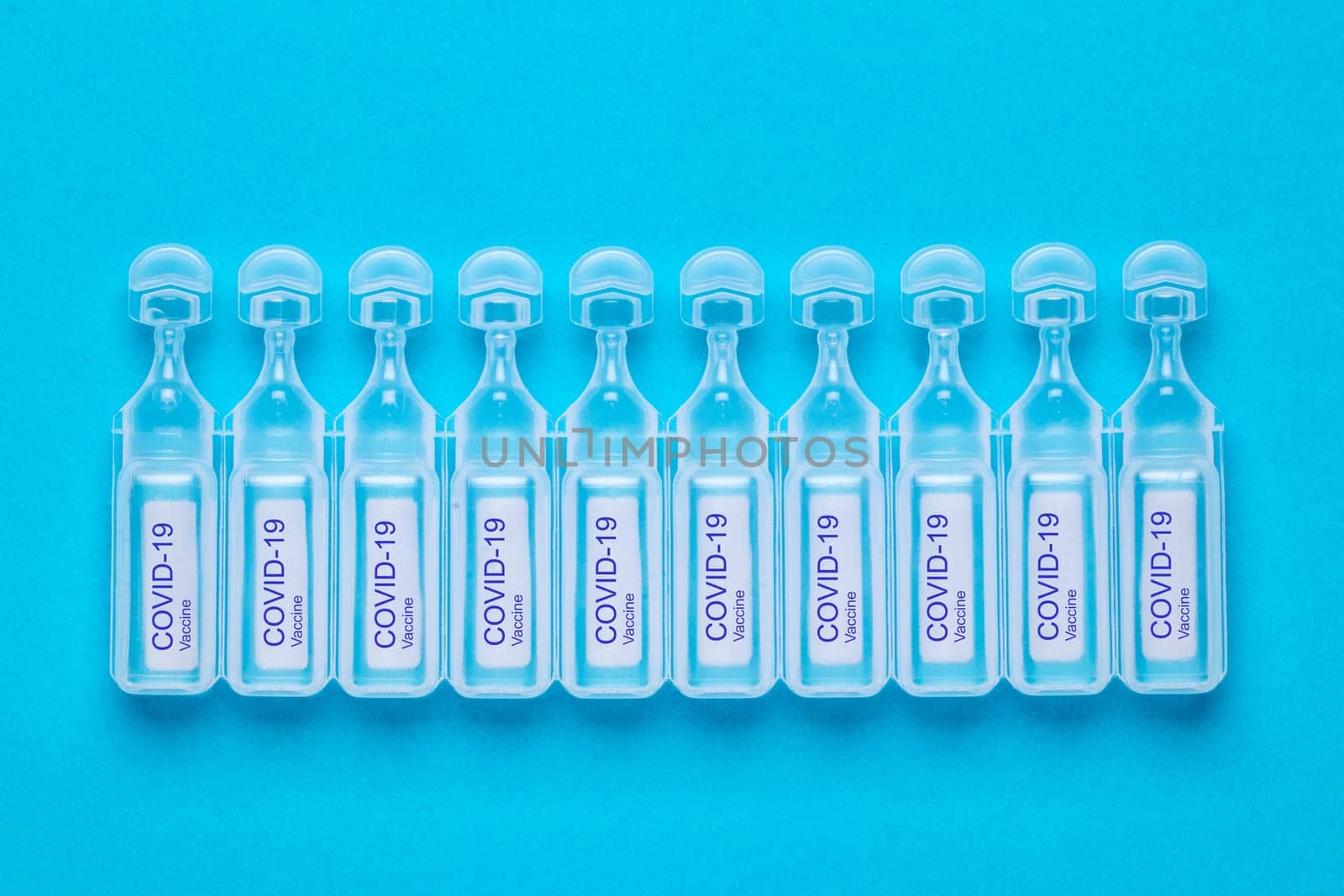 Coronavirus treatment concept. Close-up of ten ampoules with vaccine COVID-19 flat layed on a blue background. Global pandemic outbreak and healing the deadly coronavirus. Macro photograph.