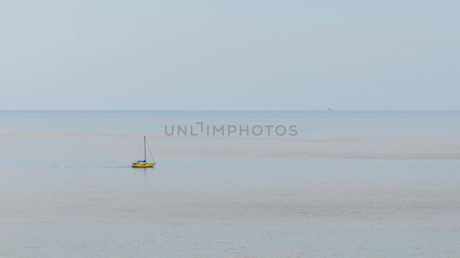 Yellow boat with its sails gathered up and stopped in a totally calm sea