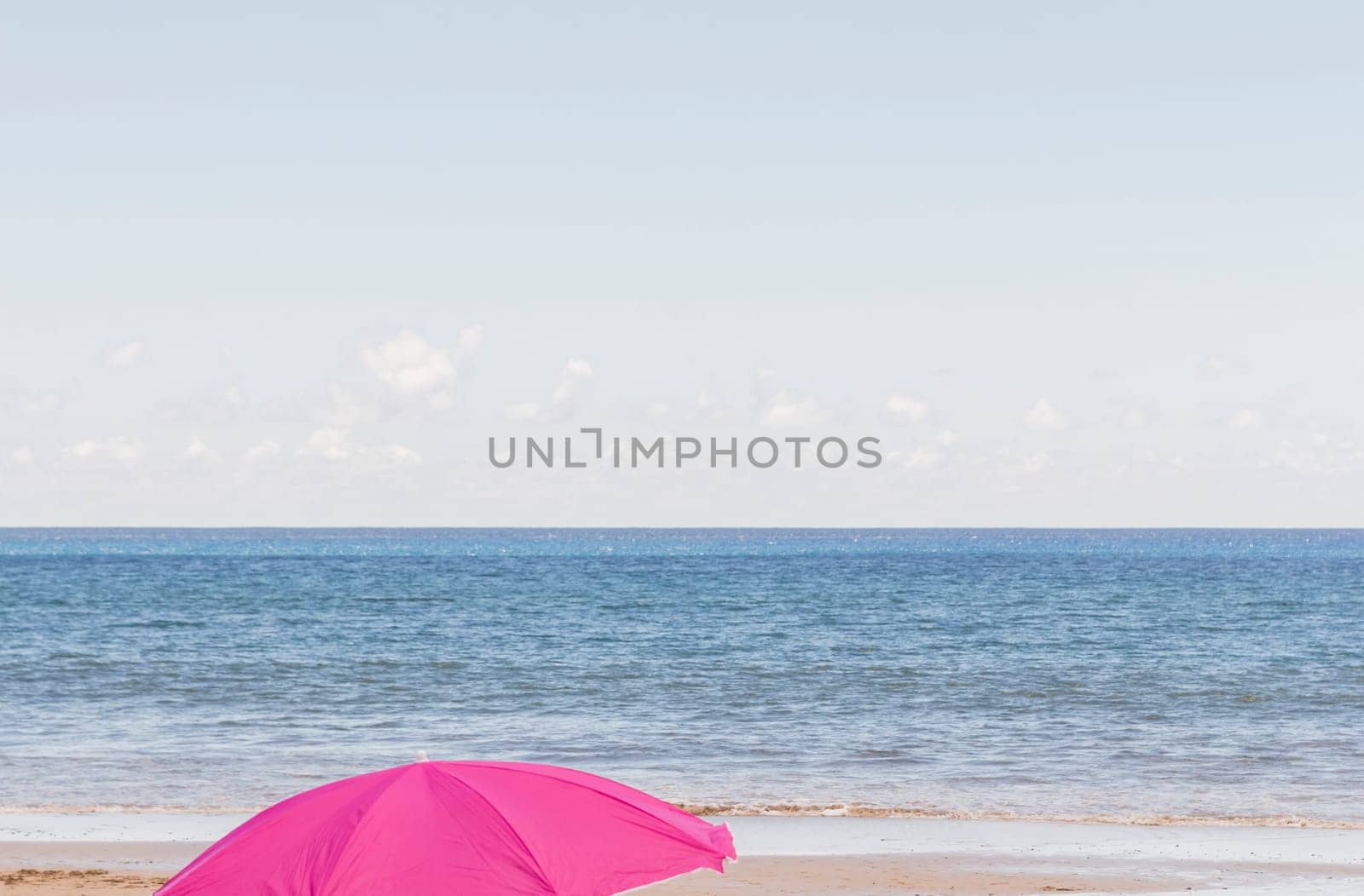 Magenta umbrella in the foreground on a lonely beach with a calm sea