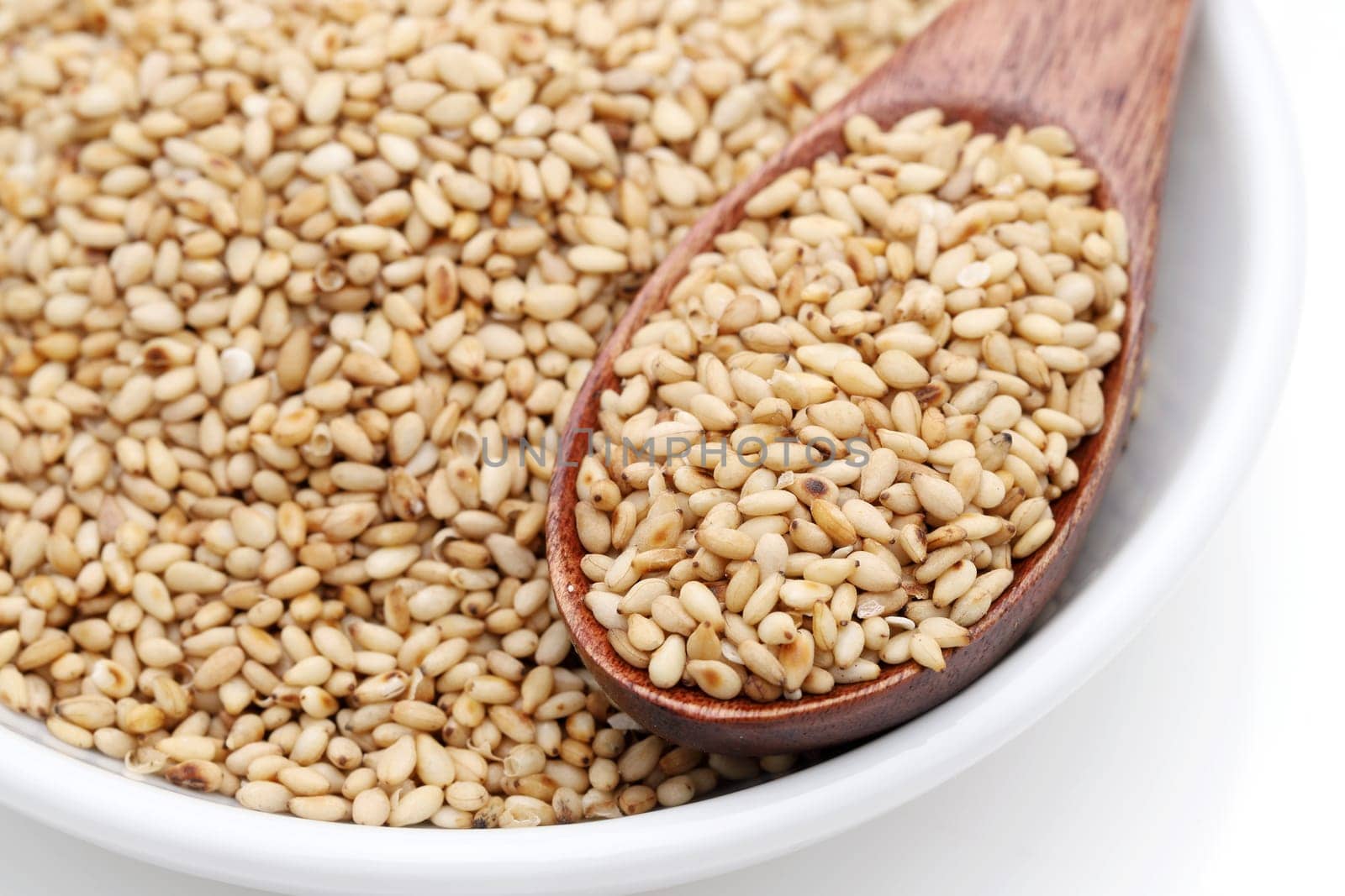 White sesame seeds with wooden spoon in a dish on white background