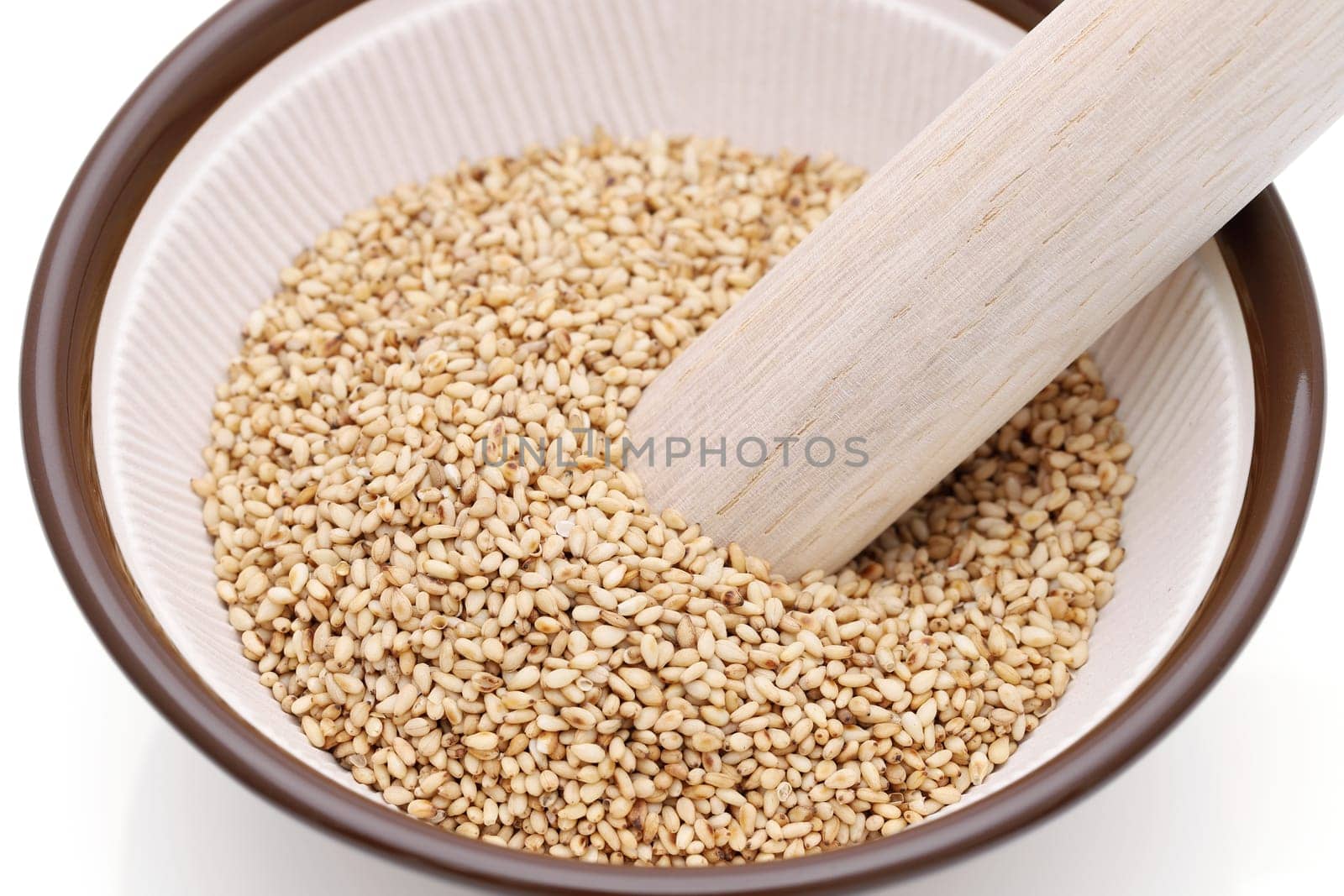 White sesame seeds with wooden pestle in a mortar on white background