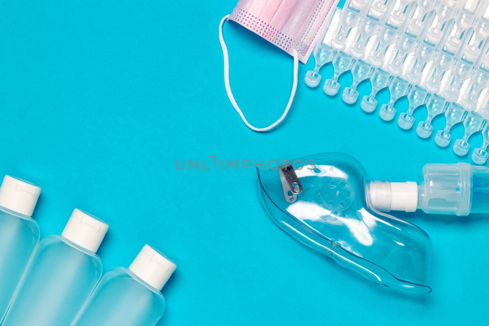 Coronavirus protective measures. Close-up of amedical face mask for treatment of the respiratory tract, ampoules, three bottles of disinfectan and a surgical mask flat layed on a blue background. Personal protective equipment. Copy space. Macro.