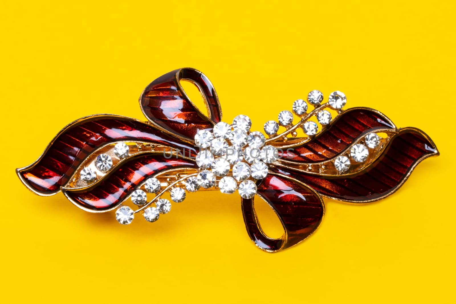 Close-up of a beautiful elegant luxurious hair clip or hair pin with rhinestones on a yellow background. Macro photograph.