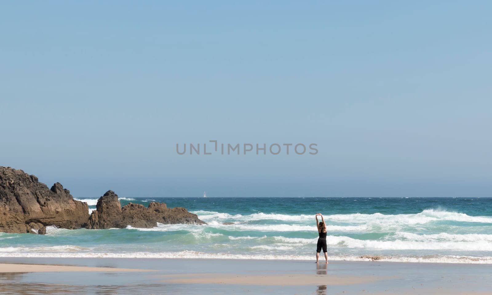 Blonde girl stretching her back as she watches the waves on the seashore