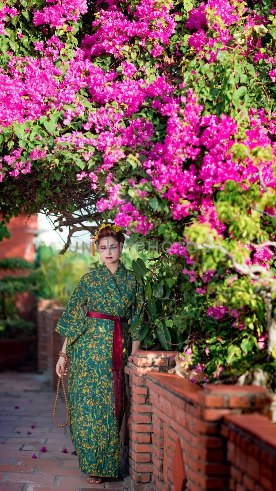 Fine art portrait of beautiful woman in Japanese Geisha style wearing kimono in a garden