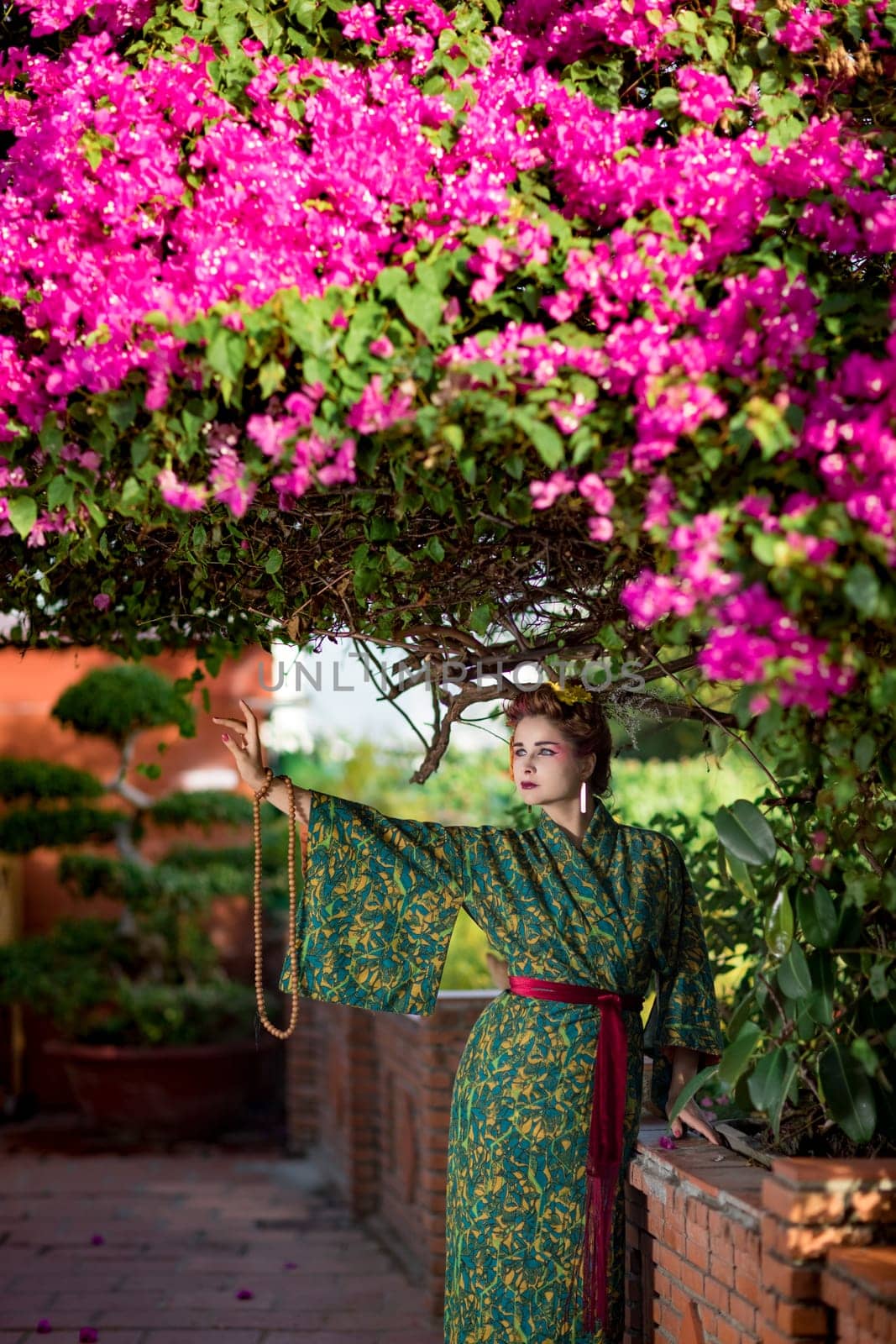 Fine art portrait of beautiful woman in Japanese Geisha style wearing kimono in a garden