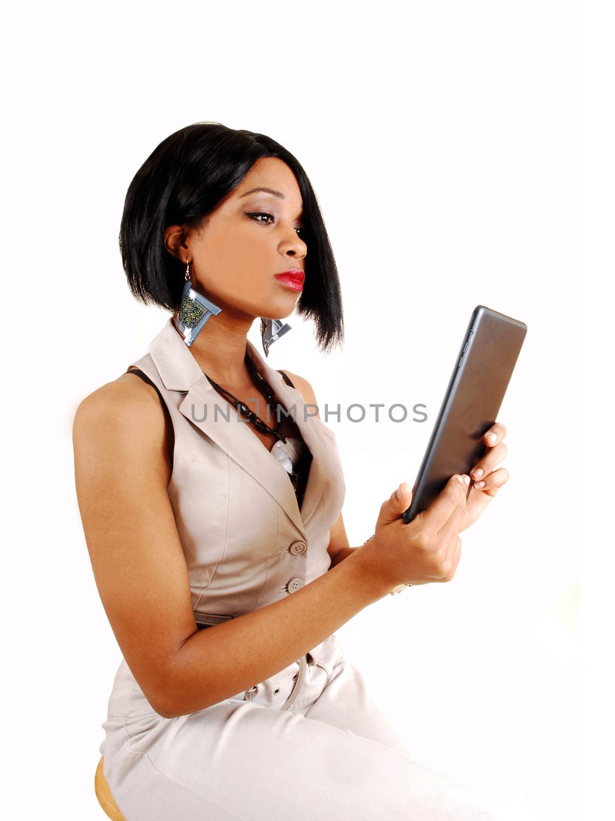 A gorgeous young woman in a white outfit sitting on a chair and working.with her tablet, isolated for white background.