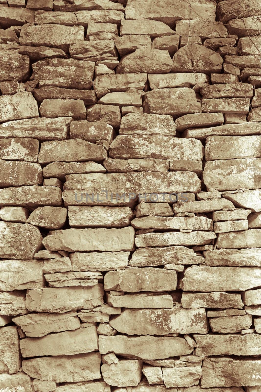 A vertical greyscale shot of an old wall made with uneven sizes of rocks