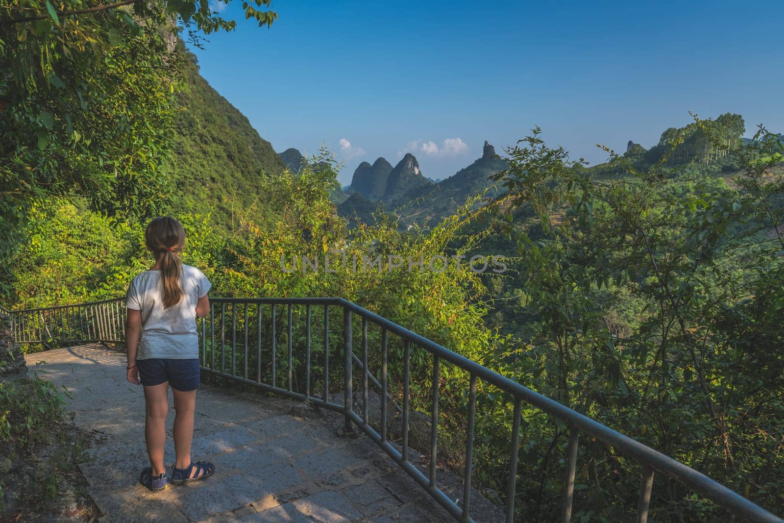 Little girl standing on the sidewalk in the middle of the mountains and enjoying the view of karst mountain scenery of Yangshuo, China