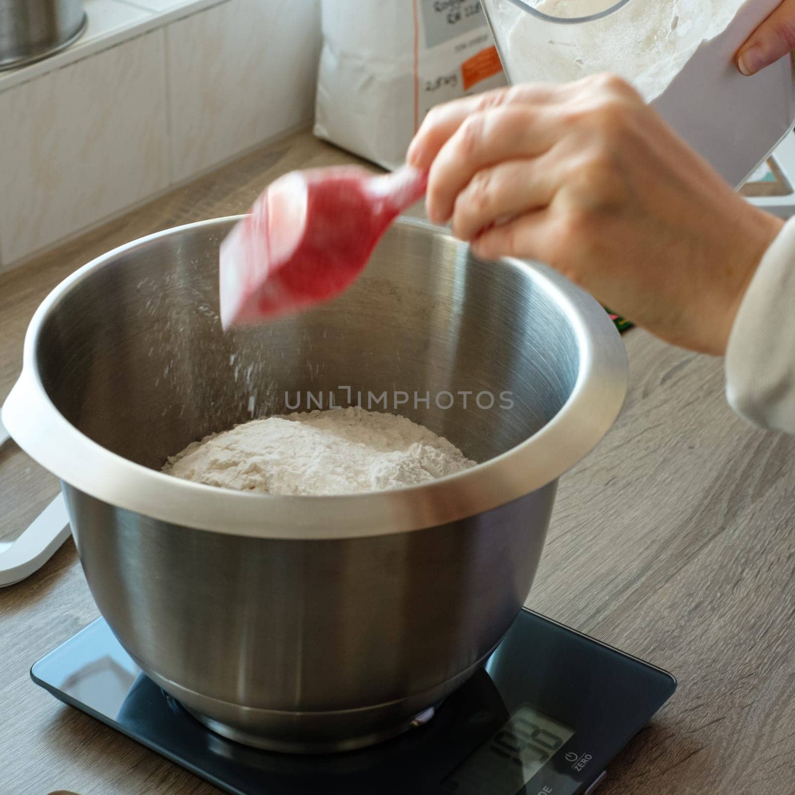 Hand is putting flour into a bowl for baking