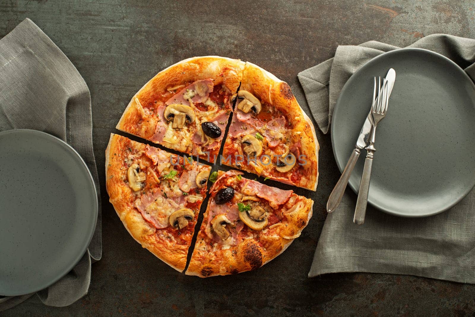 Pizza served with mozzarella cheese, ham, mushrooms, tomato sauce and fresh basil