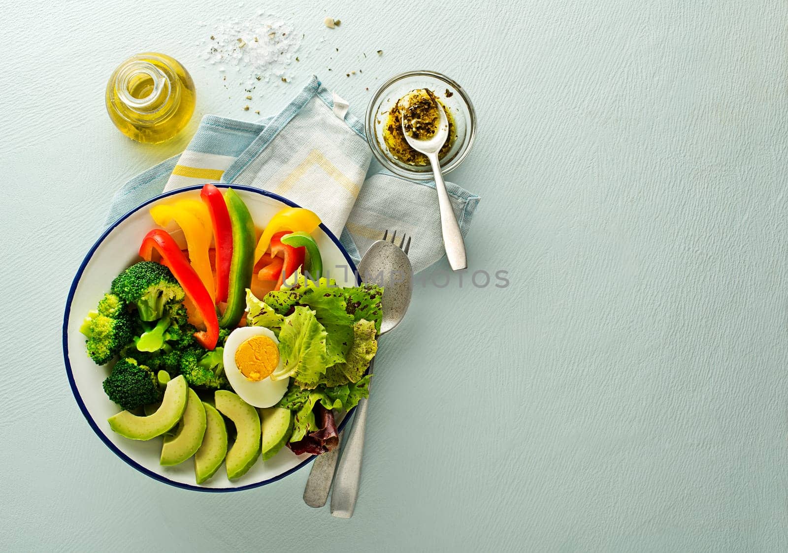 Healthy salad meal with mixed fresh vegetables, avocado and egg on blue background top view. Food and health. Healthy meal concept