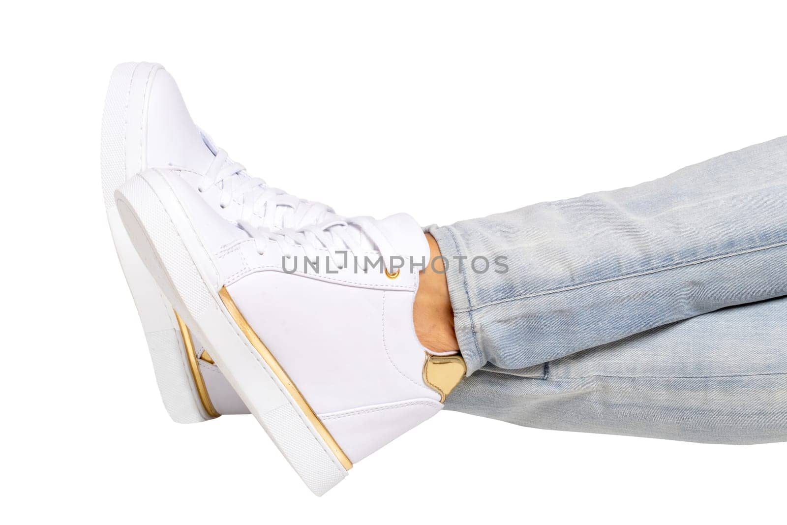 Women legs in jeans and sneakers. Woman legs in light denim pants wearing modern white sneaker. Fashionable white footwear. Macro photograph.
