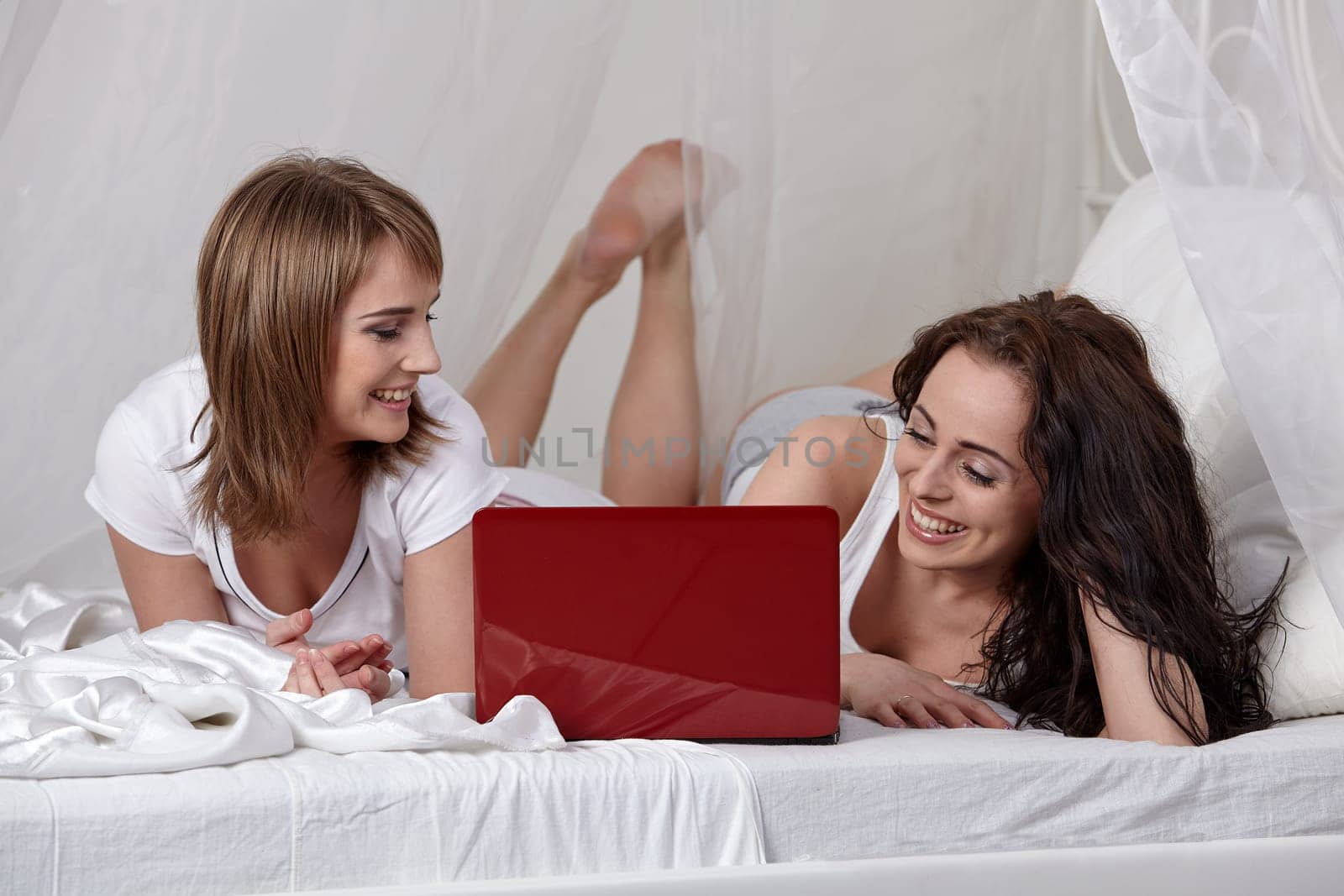 Two girlfriend with  laptop lie on the bed at home.