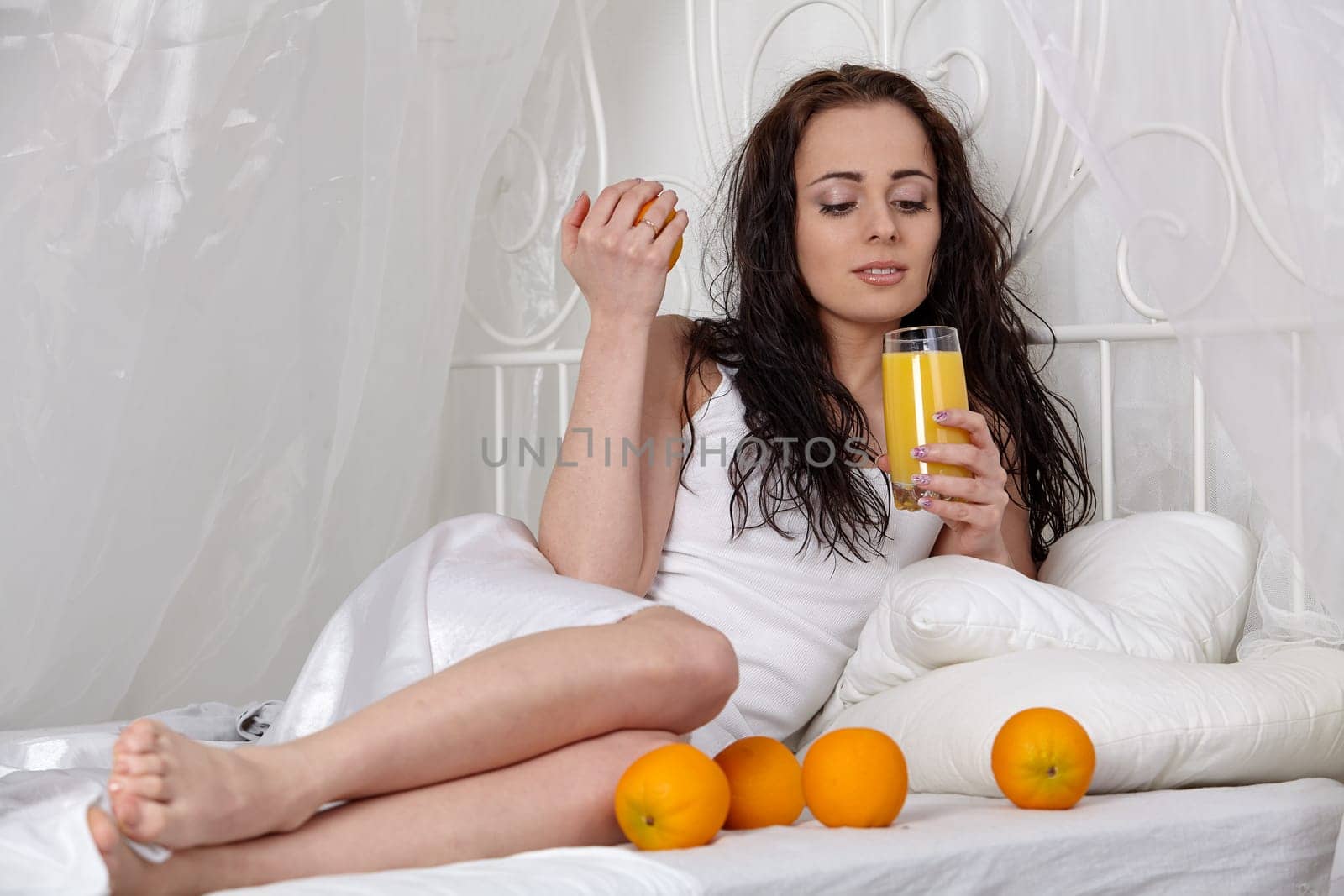 Young beautiful woman with  oranges and juice sits on a bed.  Concept  of healthy food.