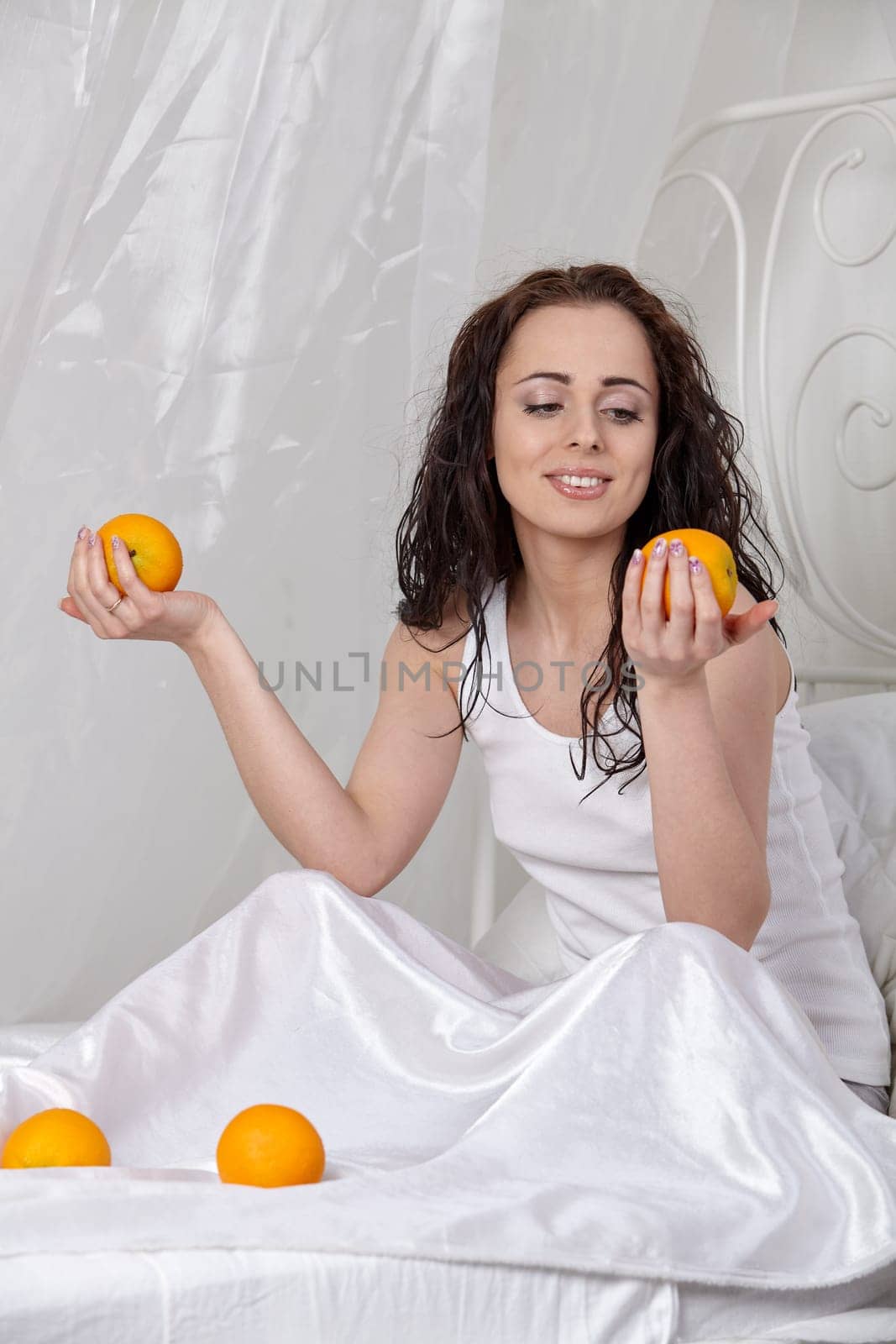 Young beautiful woman with  oranges and juice sits on a bed.  Concept  of healthy food.