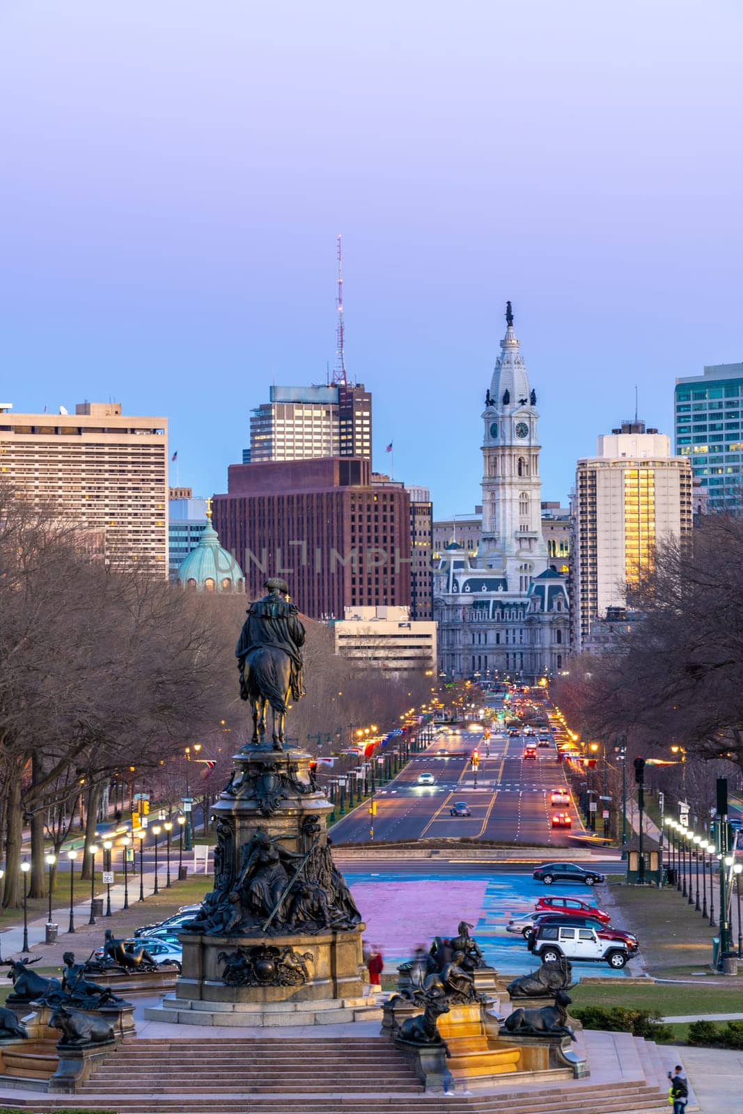 Cityscape of Philladelphia with City Hall Clock Tower and statue monument at oval park along Benjamin Franklin Parkway road in Philladelphia Center city downtown, Pennsylvania, USA. Sunset