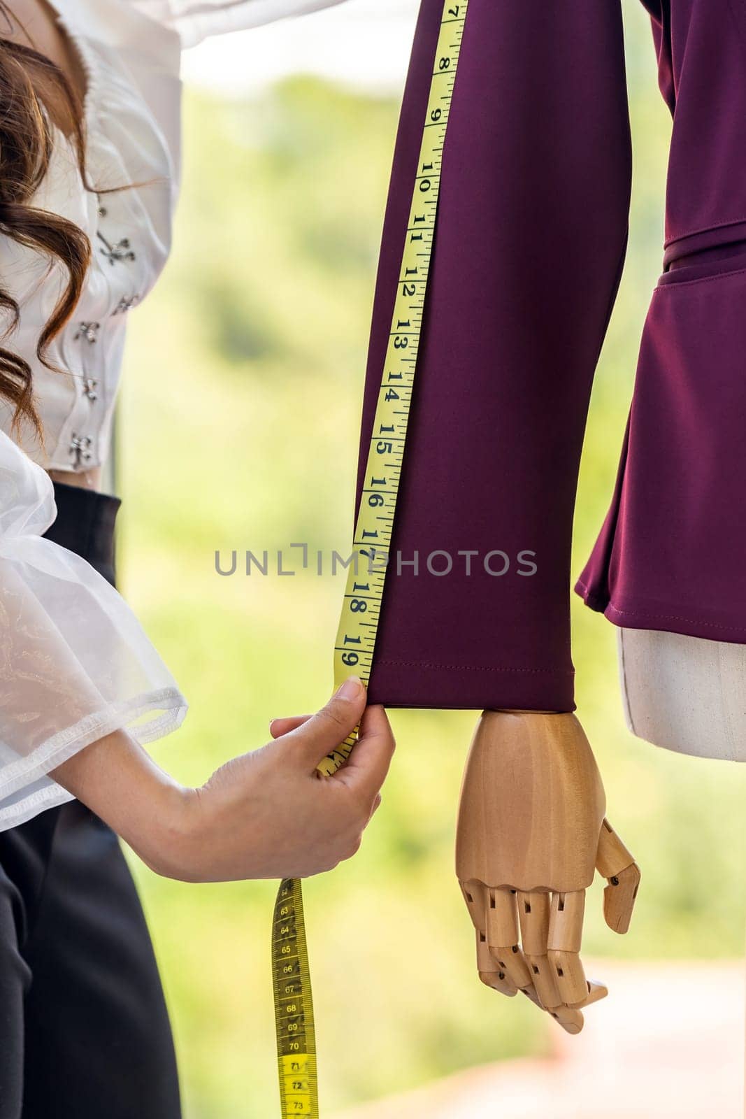 Close-up young adult asian fashion designer using measuring tape to measure suit arm at her atelier studio as sole owner. Using for entrepreneur small business startup concept.