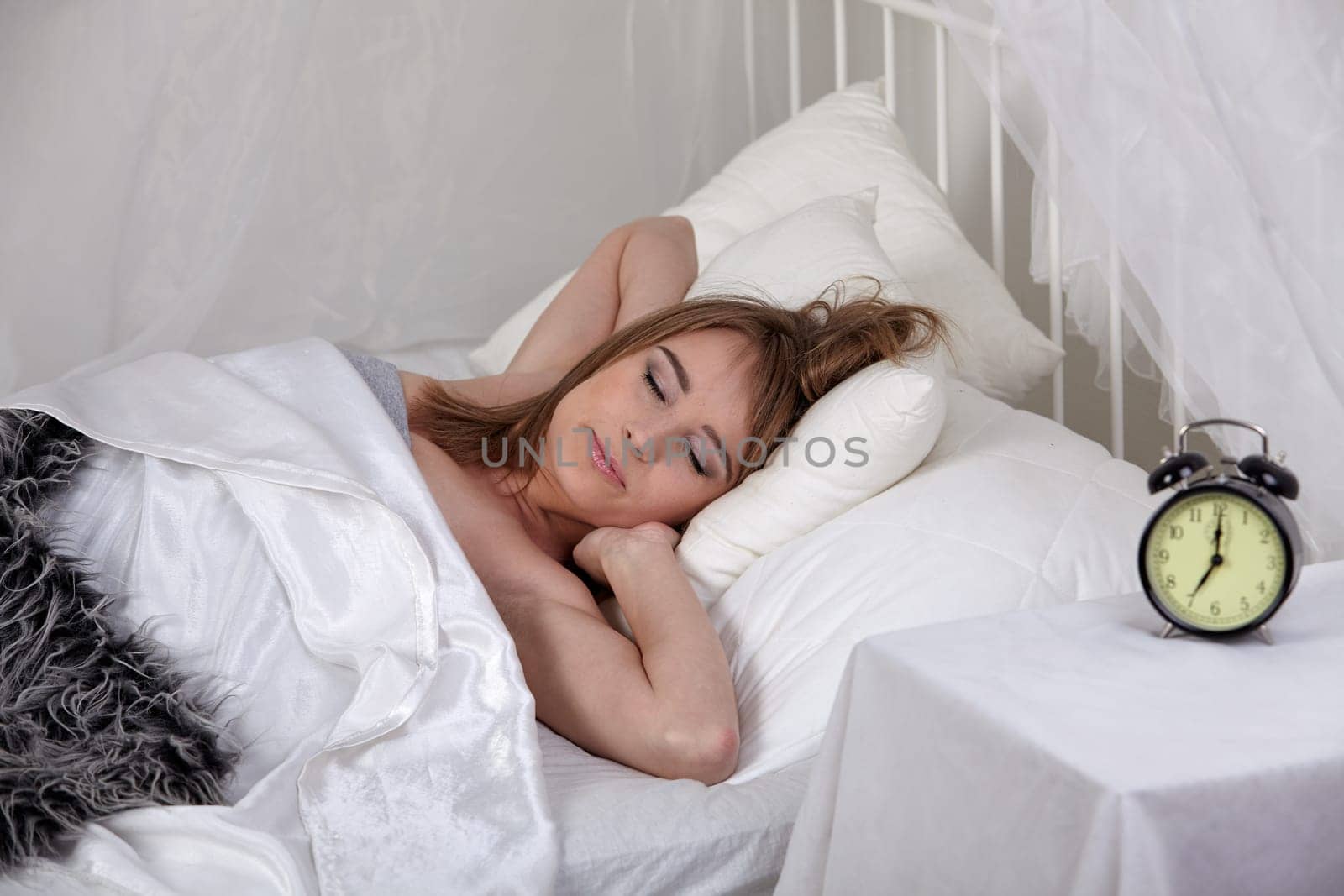 Young sleeping woman and alarm clock in bedroom at home.