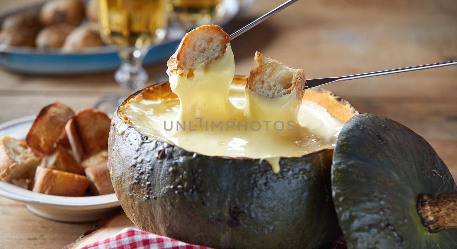 Rustic serving of cheese fondue in a roasted hollow pumpkin rind with toasted baguette for dipping in close up served with white wine
