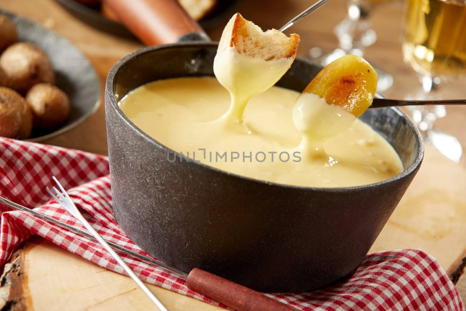 Steaming pot of creamy cheese fondue with grilled baby potatoes and toasted baguette for dipping in a close up tilted view on a rustic table