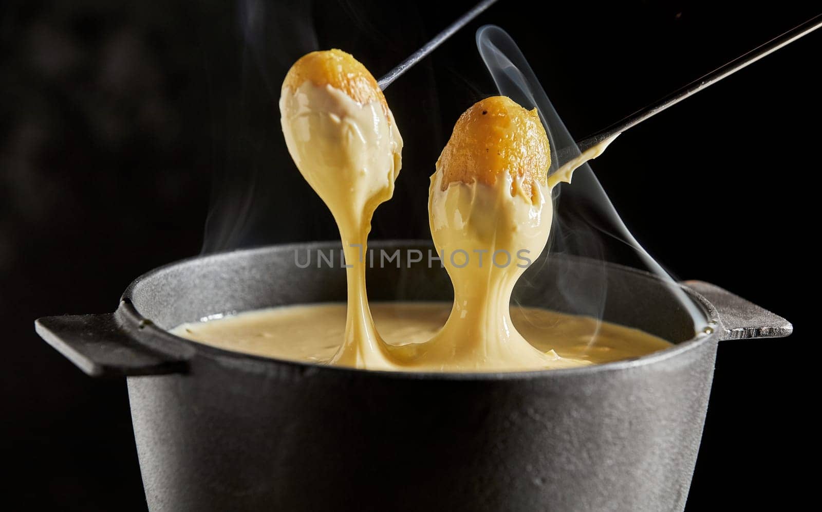 Delicious hot steaming Swiss cheese fondue served with grilled baby potatoes for dipping in close up over a dark background