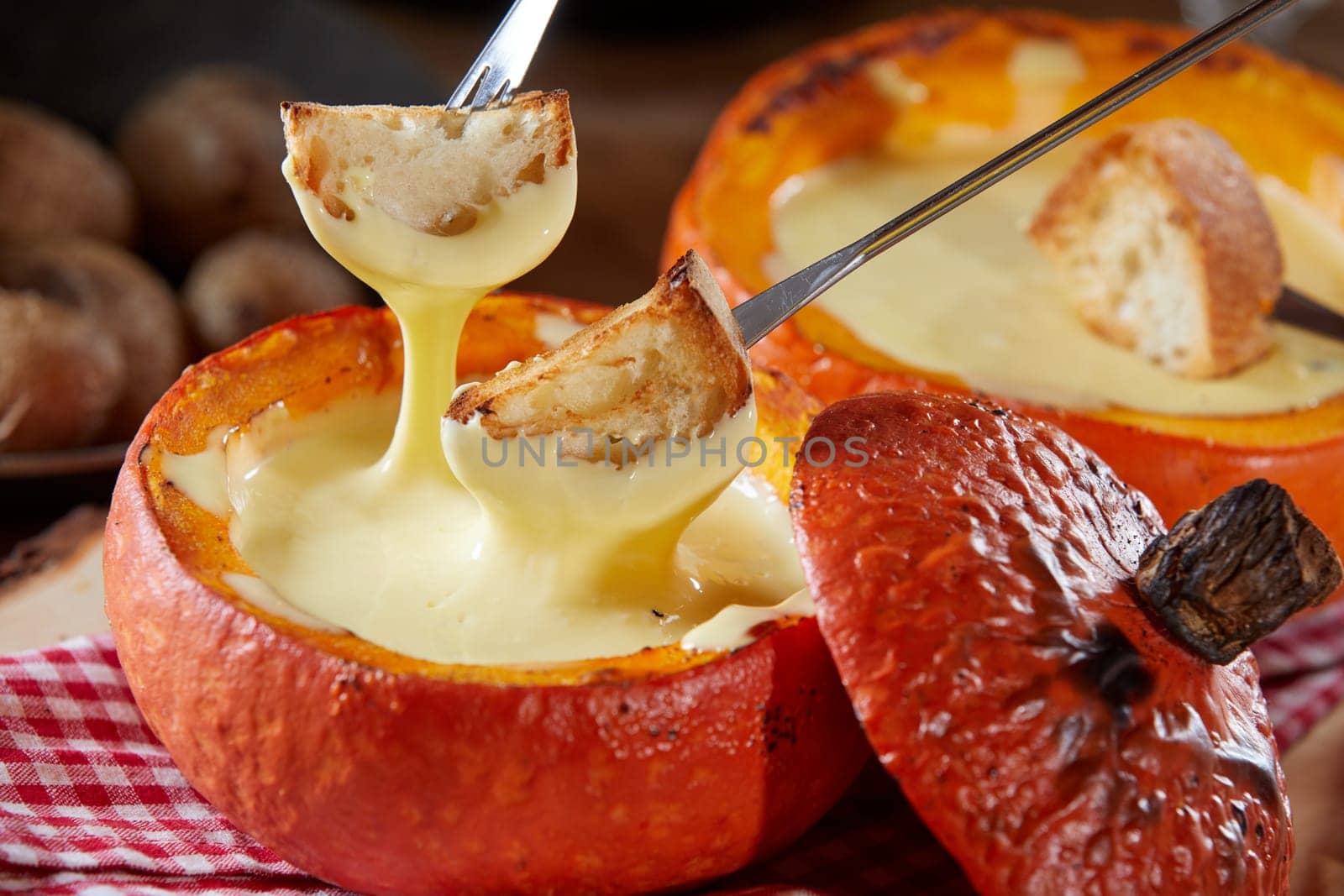Delicious raclette melted cheese fondue served in a hollowed pumpkin with toasted baguette dipping pieces on forks in close up for a tasty fall meal