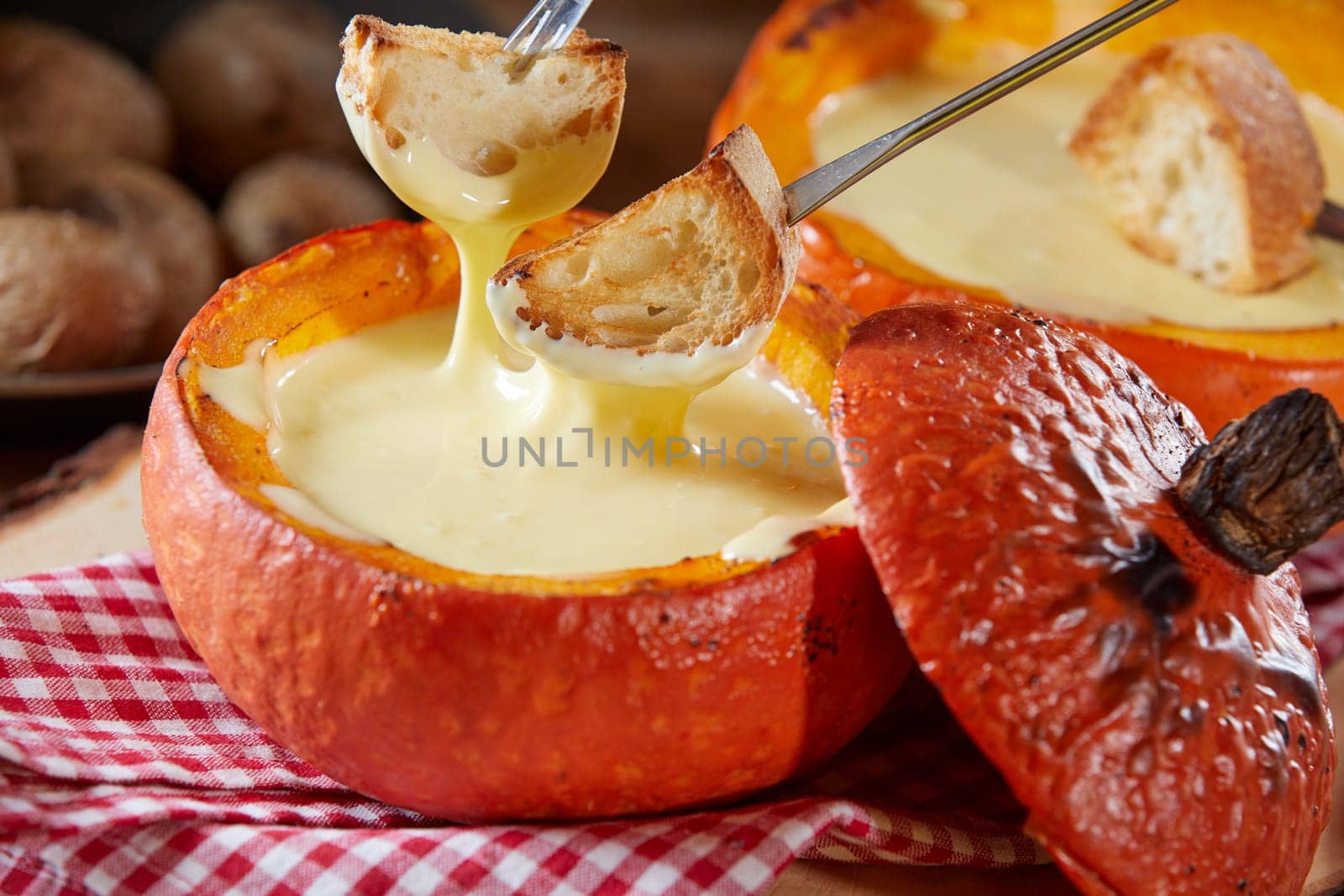 Tasty cheese fondue served in a colorful orange pumpkin rind in autumn in close up with forks dipping toasted baguette