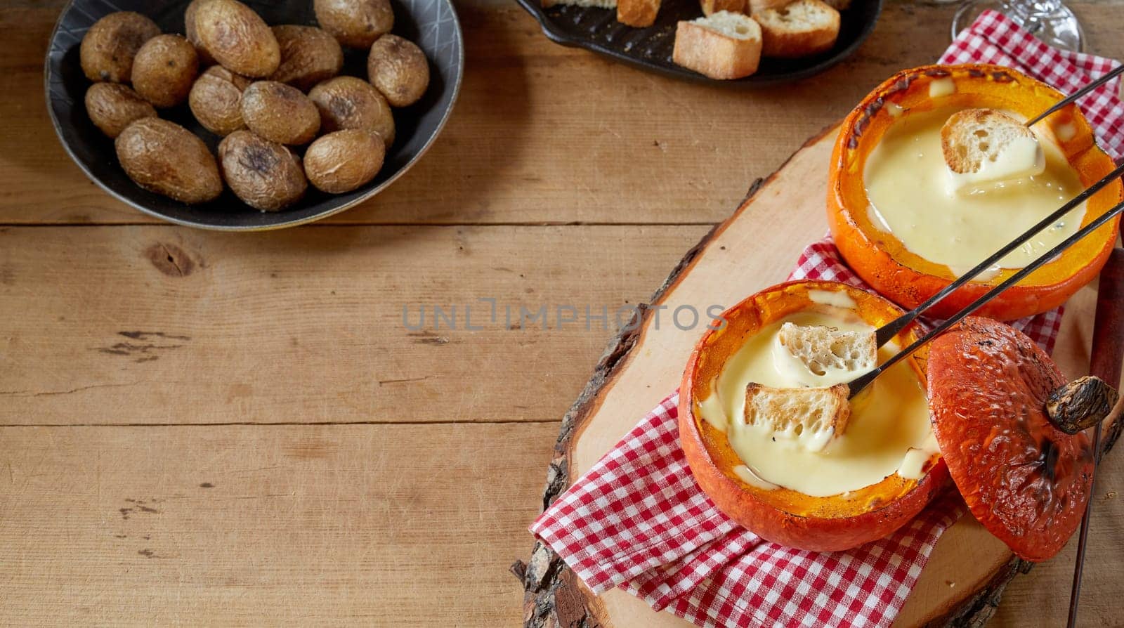 Serving of traditional Swiss cheese fondue in hollowed out roasted fall pumpkins served with baked baby potatoes and toasted baguettes for dipping in a high angle view with copy space