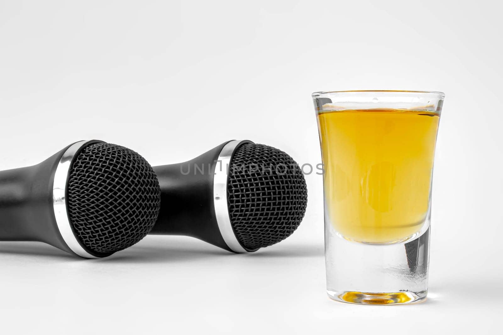 A shoot glass with liquor and two karaoke microphones on a white background