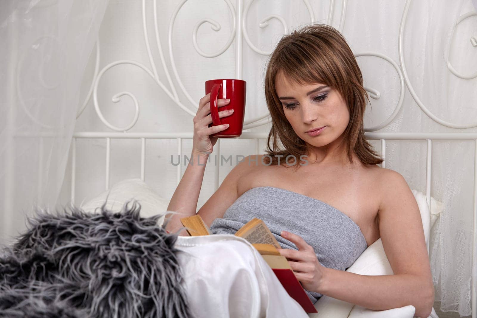 Young beautiful woman reads book in bedroom.