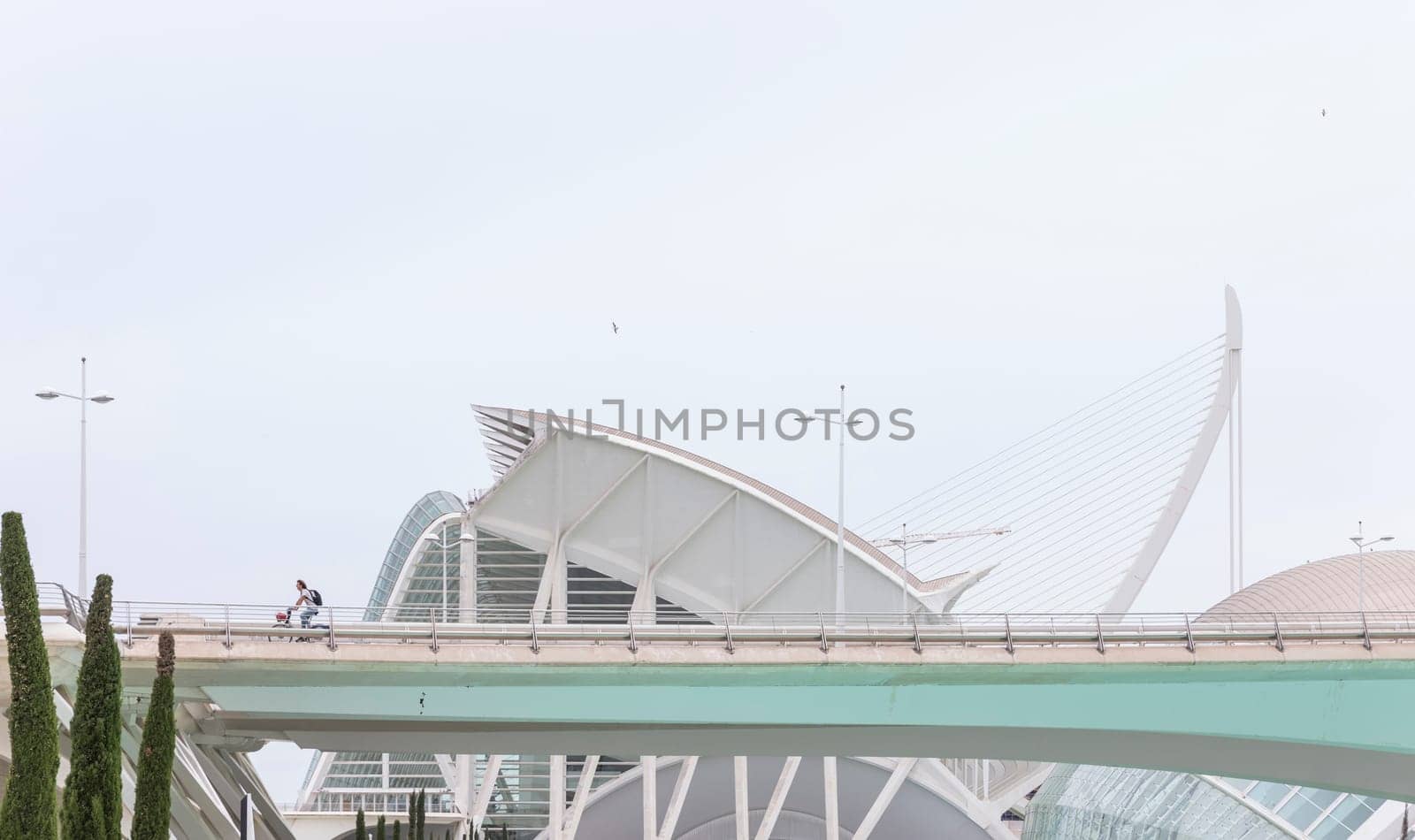 Valencia, Spain - 04, 05, 2018: A boy riding a bike over one of the bridges that crosses the City of Arts and Sciences, with the Principe Felipe Science Museum in the background.
