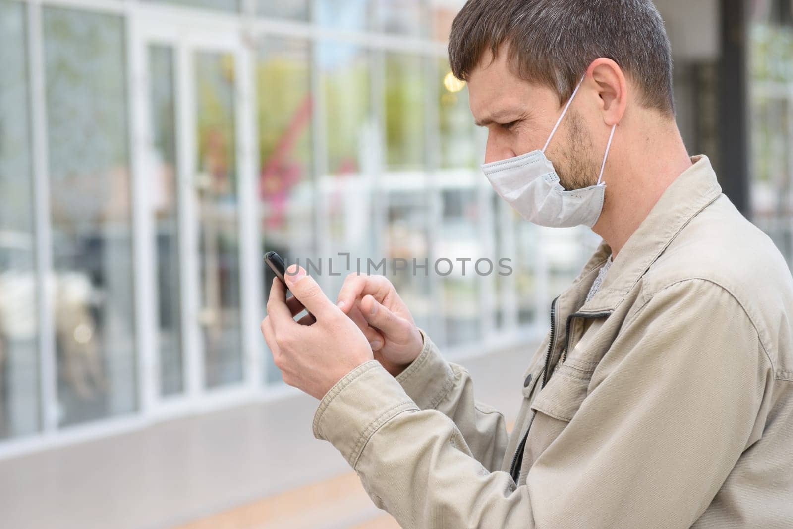 A man in a medical mask dials a number in a mobile phone, close-up