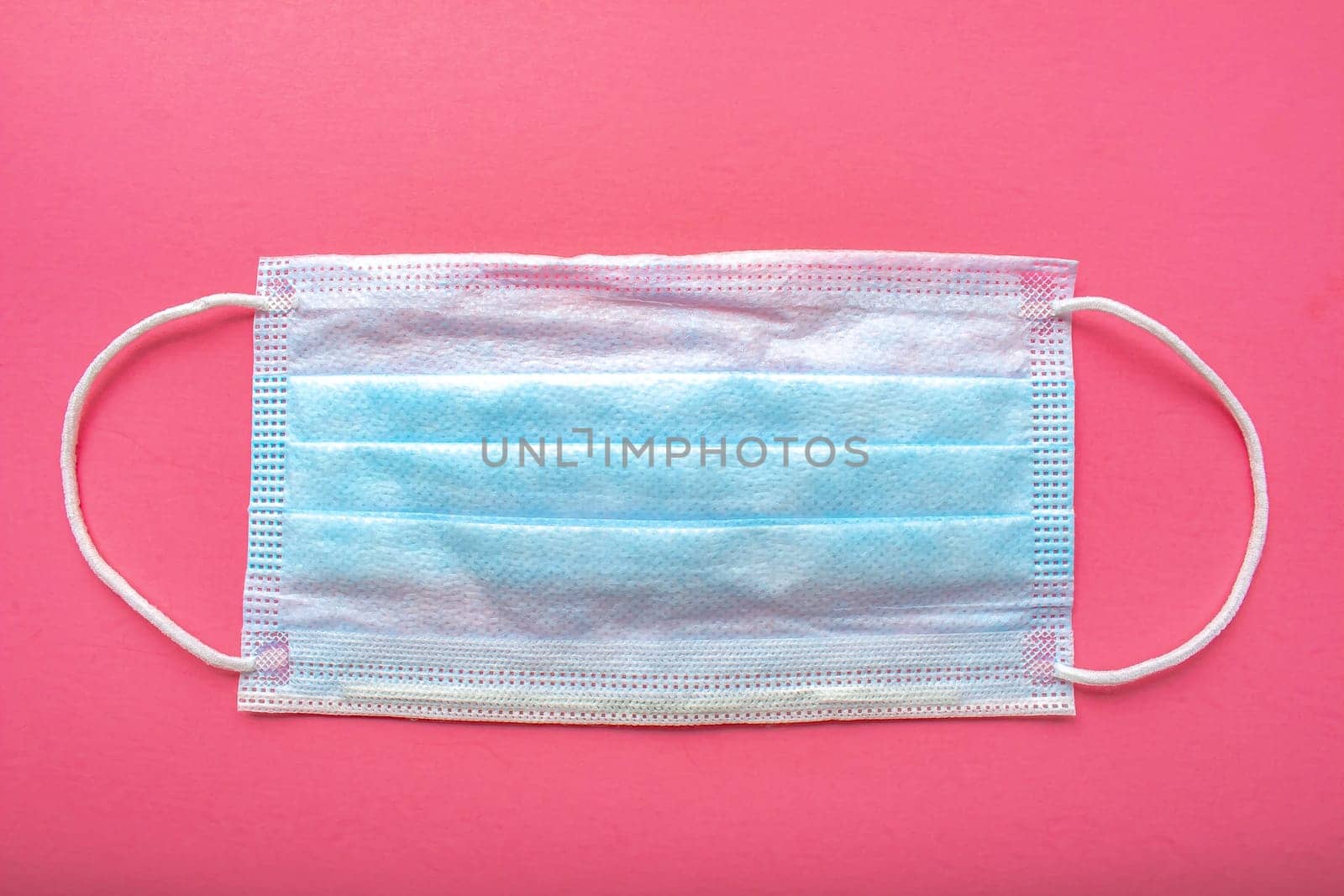 A medical surgical face mask on a pink background