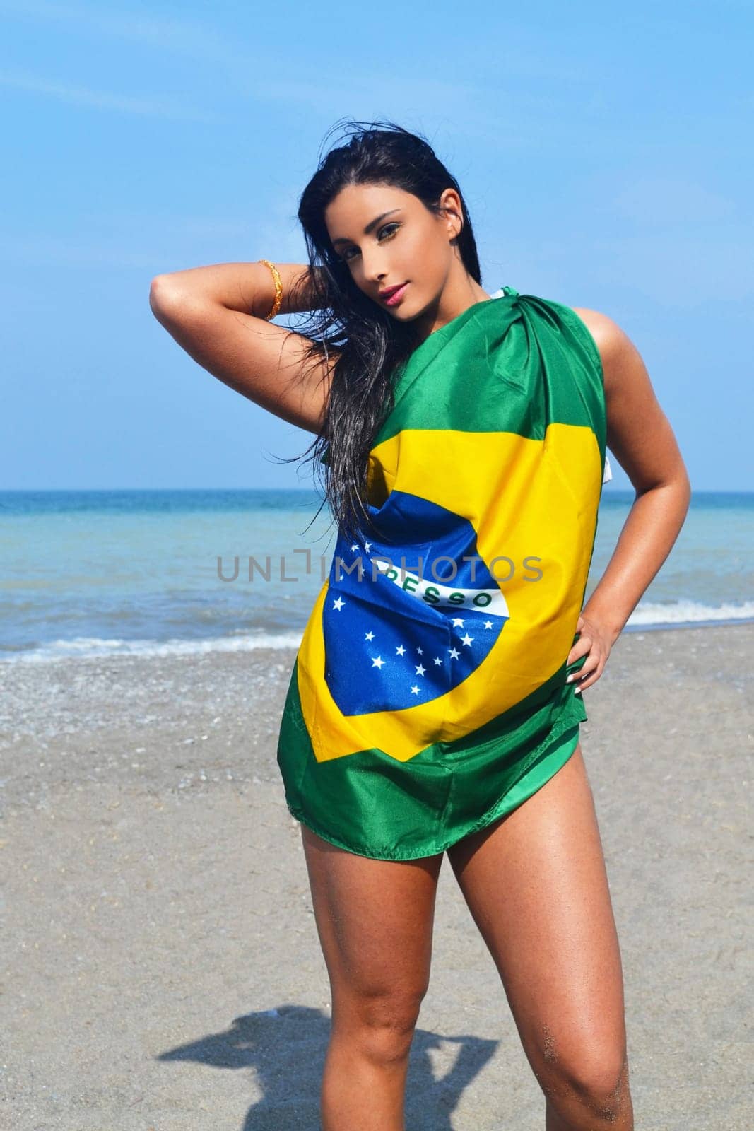 Beautiful young woman standing on the beach covered in a Brazilian flag.with her long black hair.