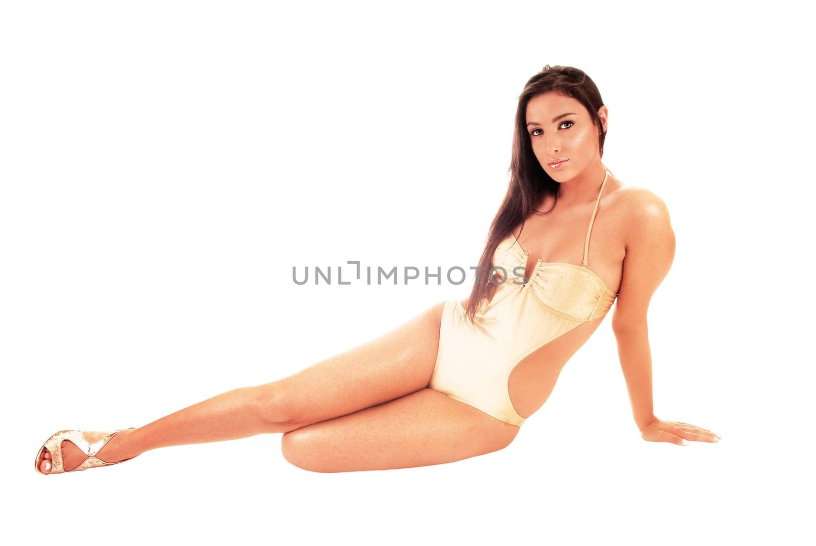 A beautiful young woman in a beige swimsuit sitting in the studio on the.floor with her long black hair, isolated for white background.