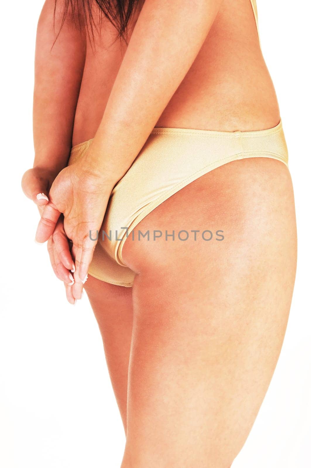 A slim woman standing from the back in a beige swimsuit with her hands.over her bottom, body part, isolated for white background.