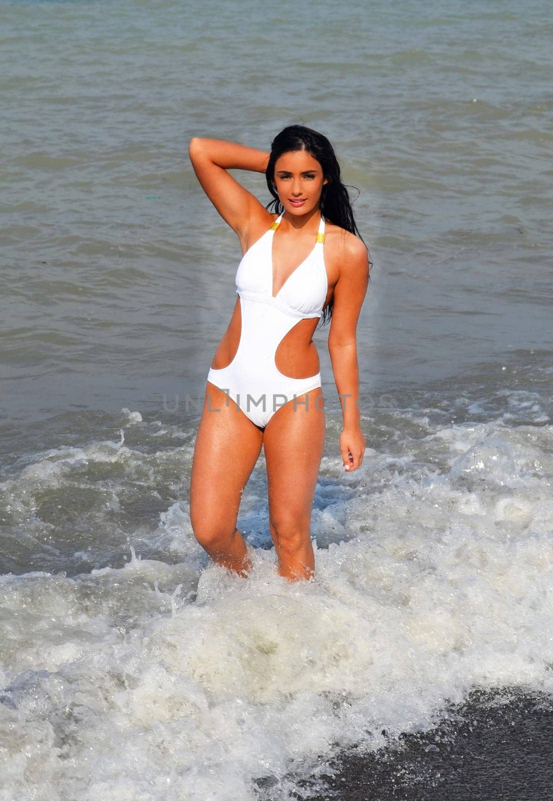 Beautiful young woman enjoying standing in a white swimsuit in the ocean.in the waves, whit her long black hair.