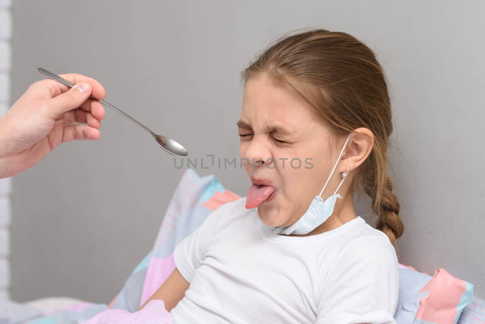 The girl frowns at the medicine given to her and pulled out her tongue