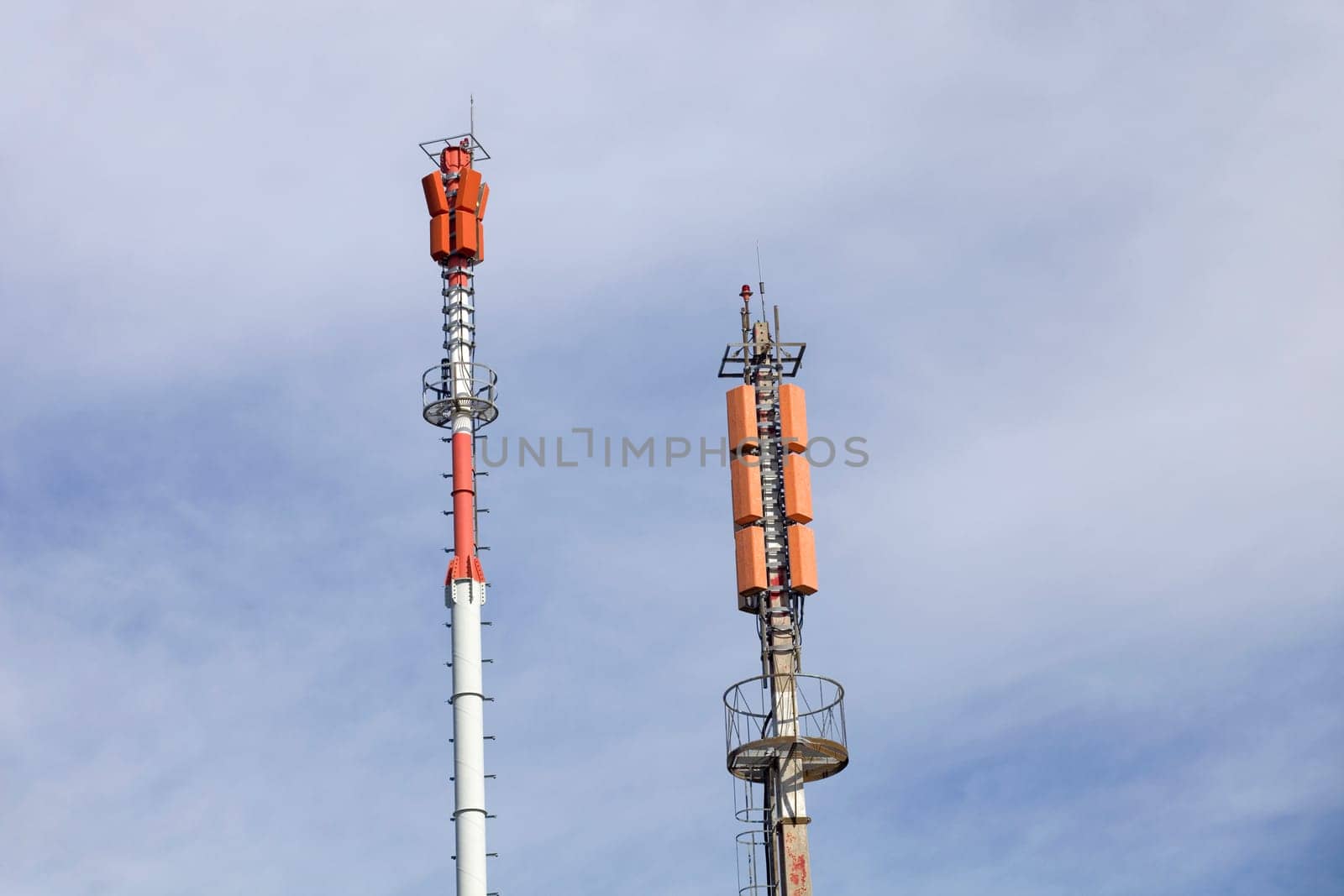 Two towers of communications with different antennas under blue sky.